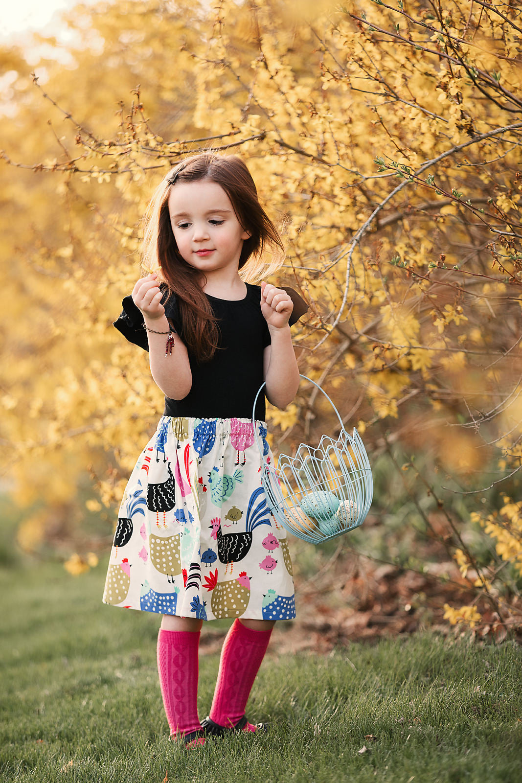 Little girl wearing a chicken print skirt with black, blue and pink chicken on an off white skirt base.