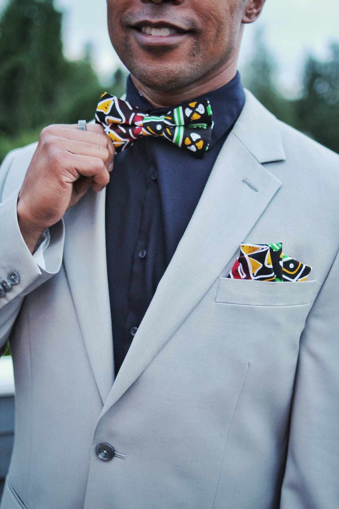 African American man wearing a grey suit and is wearing our Black multi color Reggae bow tie and pocket square