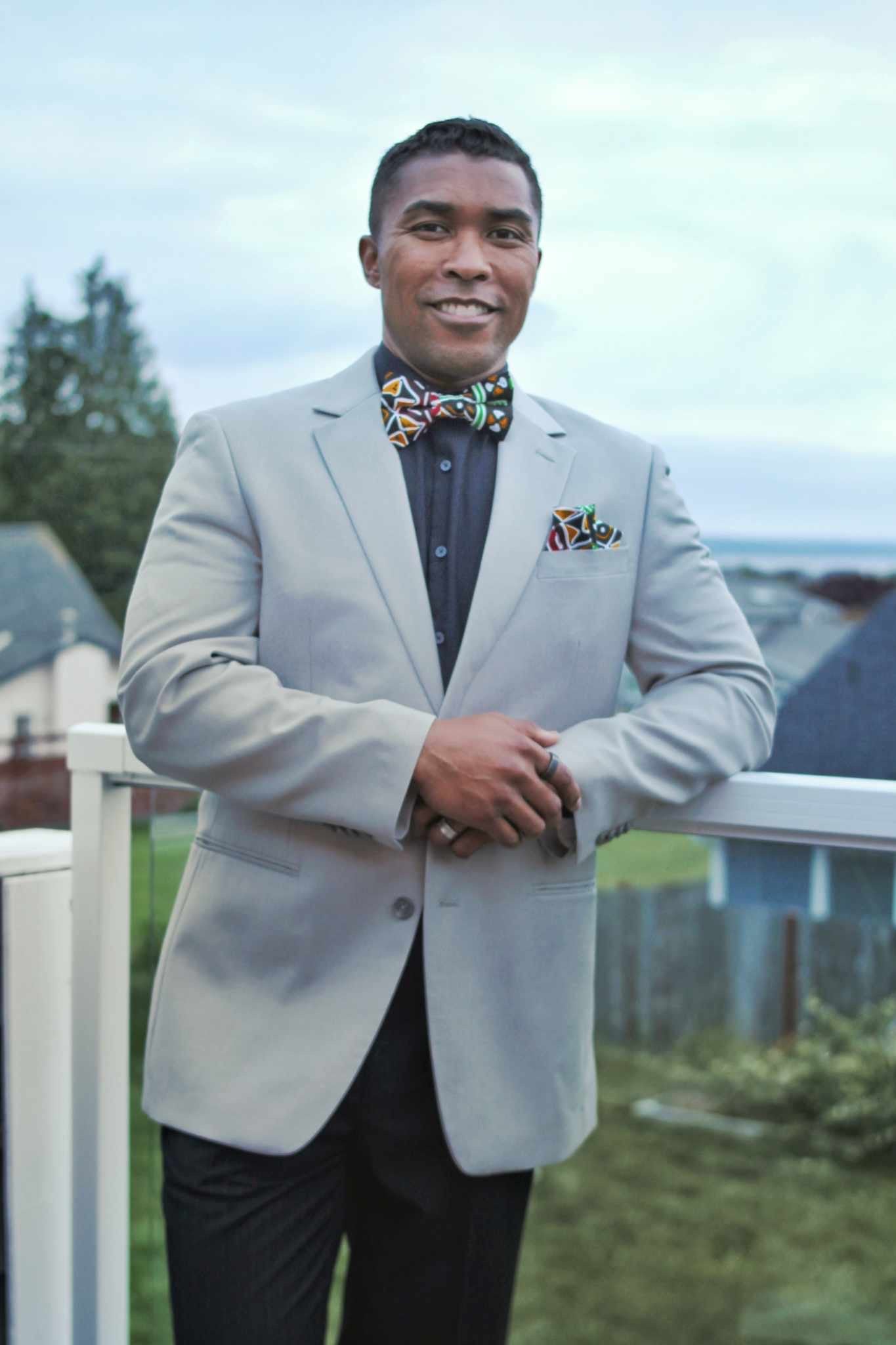 African American man wearing a grey suit and is wearing our Black multi color Reggae bow tie and pocket square