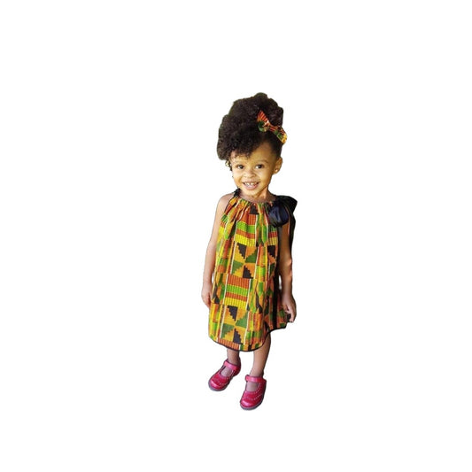 African American little girl wearing a kente pillowcase dress with black satin ribbon for straps. The hem of the dress has black bias tape.