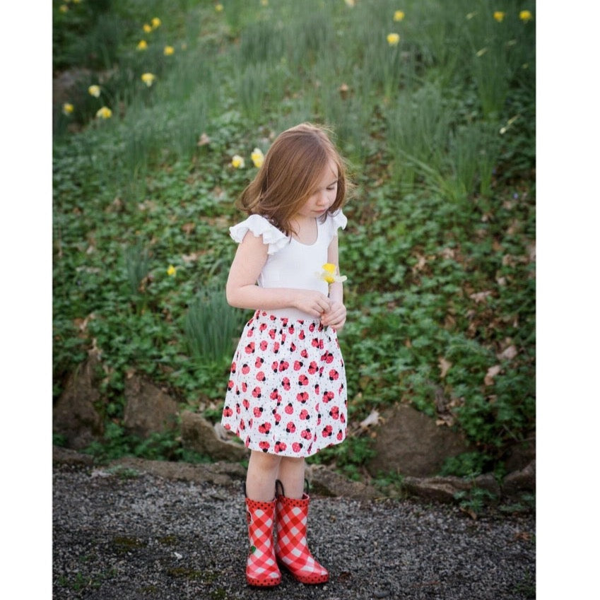Caucasian little girl wearing a white skirt with red ladybug s. The skirt has elastic waist and is about knee lenthM