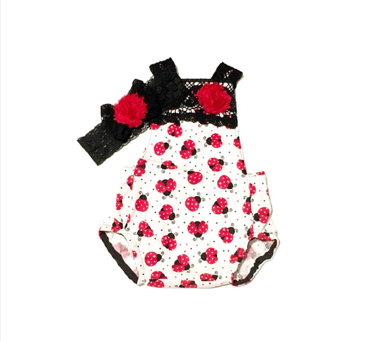 White with red Ladybug baby romper wiwith black lace trimming and a red flower. Comes with a matching blade lace and red flower headband. 