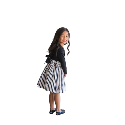 A gorgeous Asian little girl wearing a black and white striped suspender skirt that ties in the back. 