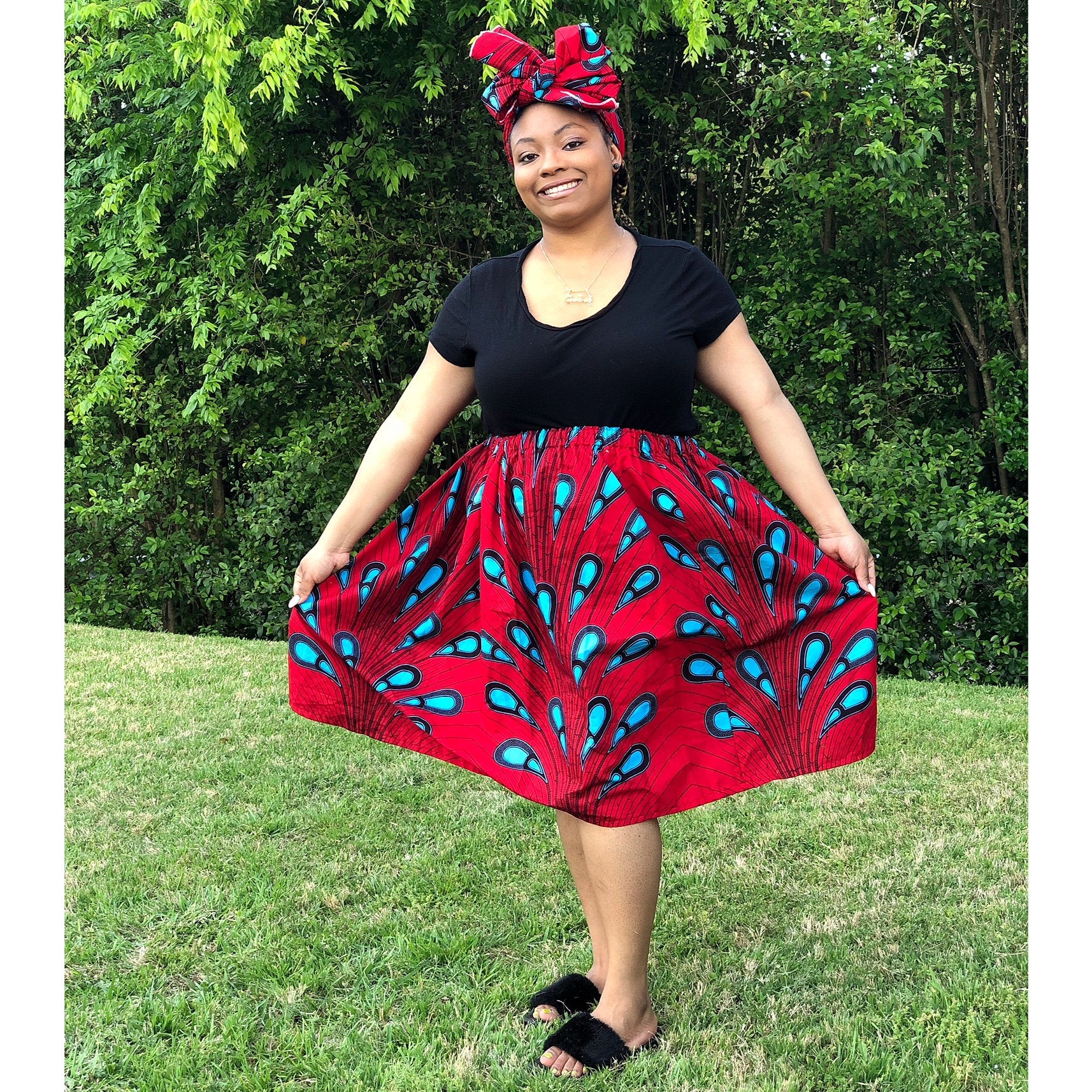 African American woman wearing an African print skirt set in red with blue print. The skirt set includes a matching headwrap. 
